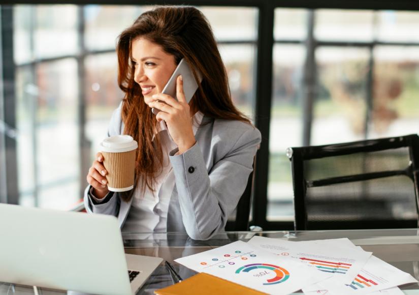 A photo of a strong female entrepreneur working away on her laptop, drinking coffee and taking on the phone while she is unlocking her potential