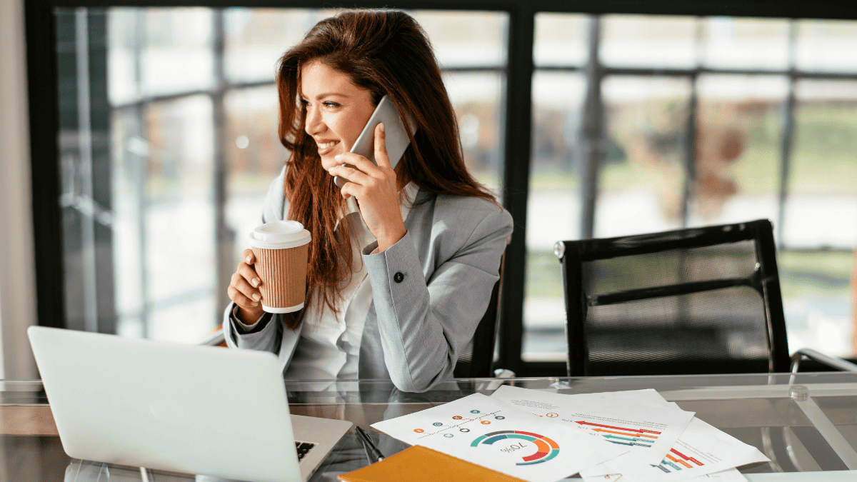 A photo of a strong female entrepreneur working away on her laptop, drinking coffee and taking on the phone while she is unlocking her potential